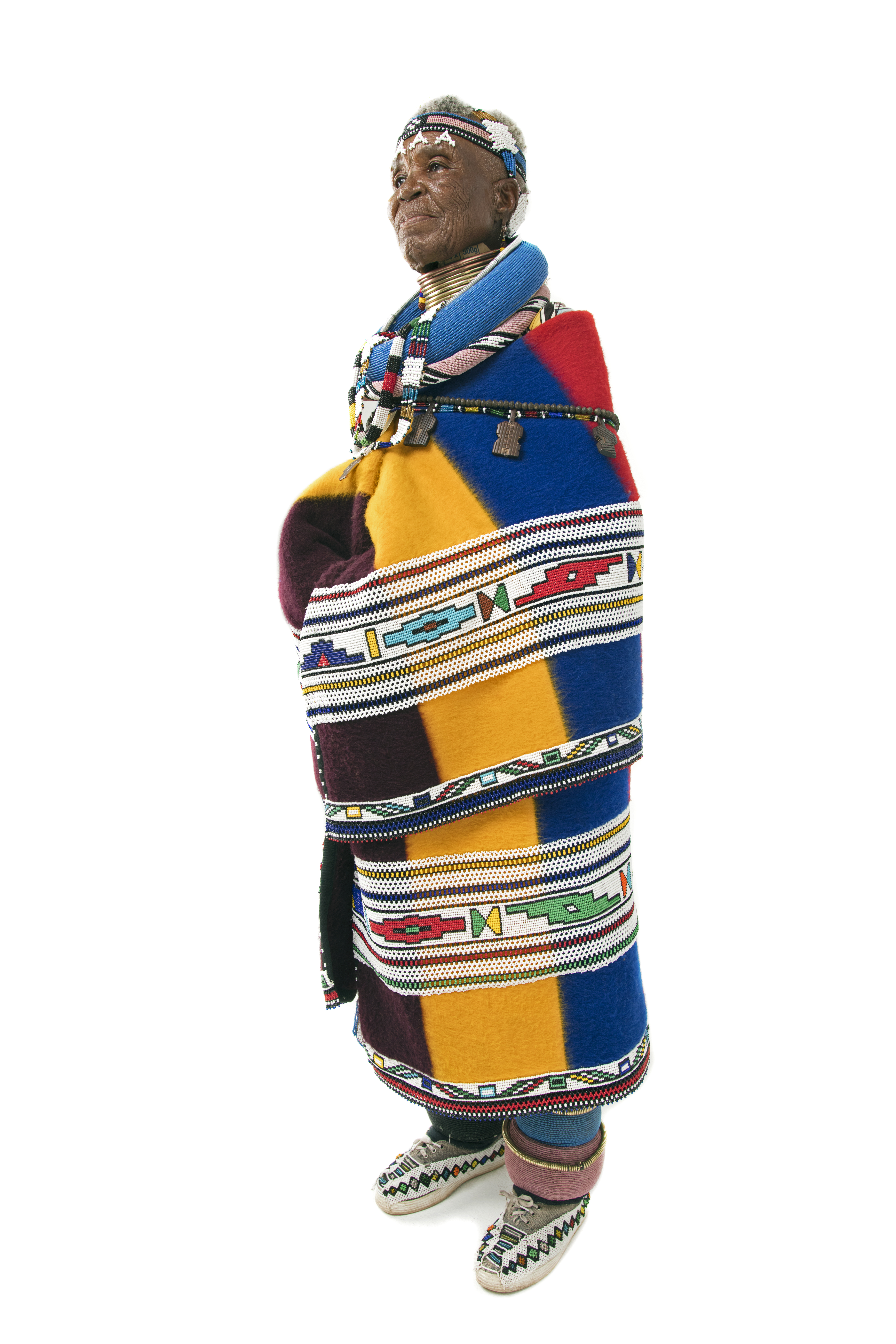 Dr Esther Mahlangu standing in full traditional Ndebele regalia, full-body profile portrait by Clint Strydom