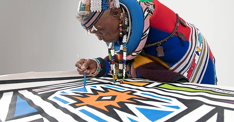Dr Esther Mahlangu painting a mural canvas, side profile, photographed by Clint Strydom