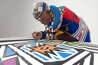 Side-profile of Esther Mahlangu painting a mural canvas, by Clint Strydom, 2018