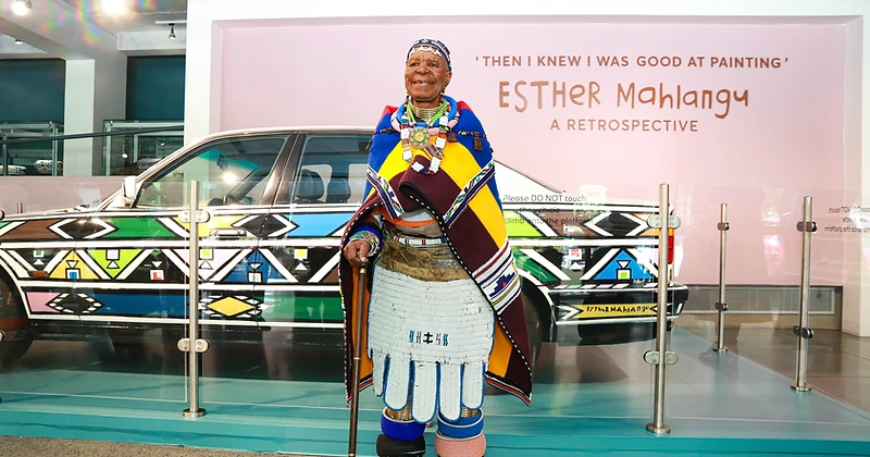 Dr Esther Mahlangu standing before her hand-painted BMW Art Car at the 'Then I Knew I Was Good at Painting' retrospective at Wits Art Museum