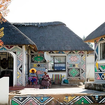 Two women before the thatched Ndebele house bearing the Dr Esther Mahlangu sign, by Clint Strydom