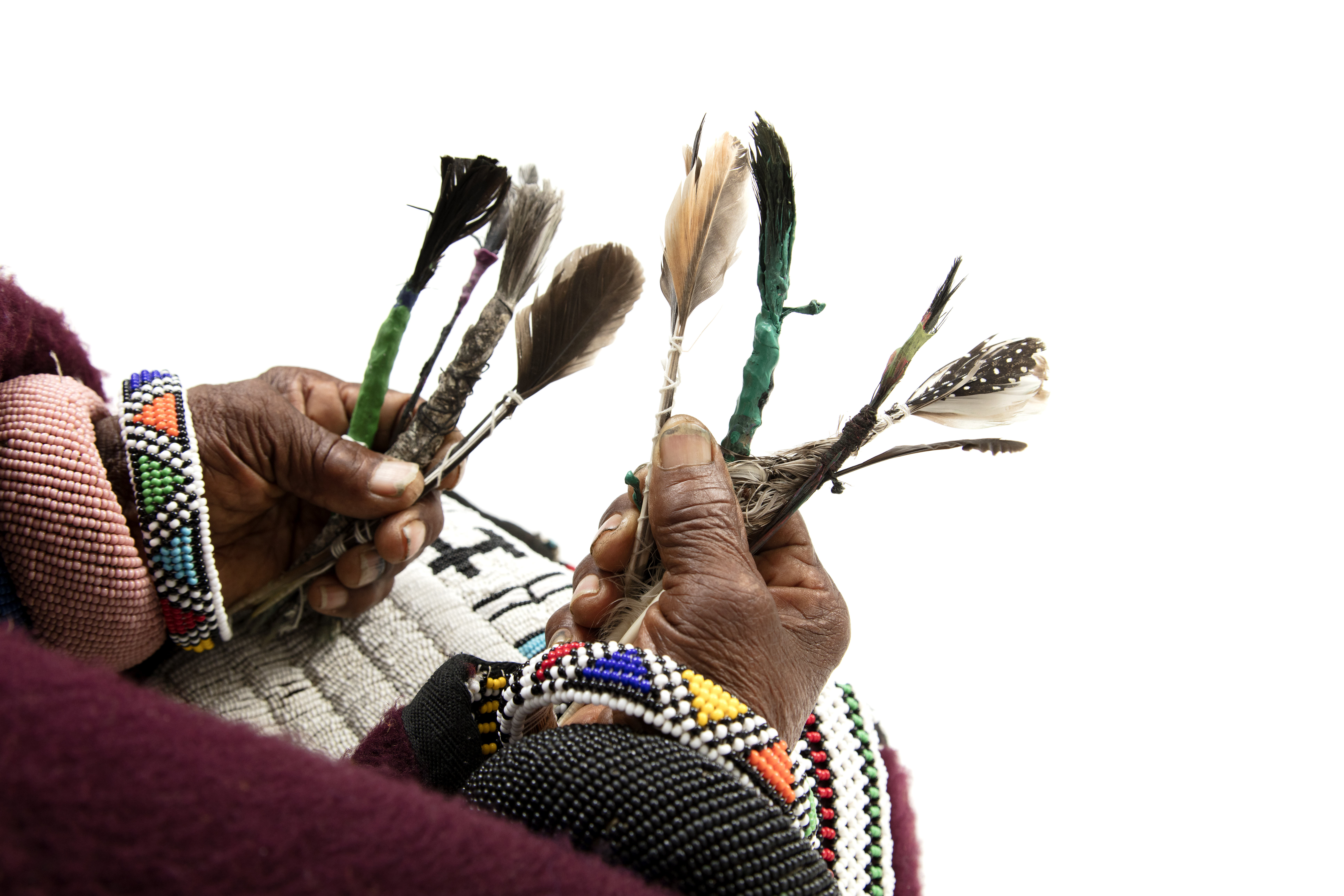 Hands holding handmade feather brushes with beaded bracelets — Dr Esther Mahlangu's first brushstrokes