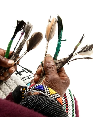 Hands holding handmade feather brushes with beaded bracelets — Dr Esther Mahlangu's first brushstrokes