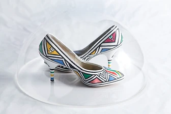 Ndebele-painted high-heeled court shoes under an acrylic dome, 2003
