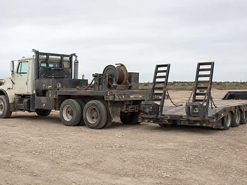 Heavy-duty flatbed truck with loading ramps parked on a gravel lot.