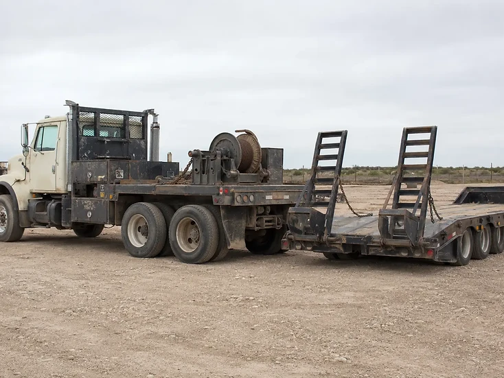 Heavy-duty flatbed truck with loading ramps parked on a gravel lot.