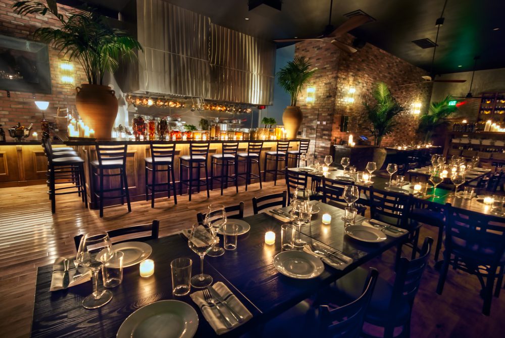 The restaurant's dining room with dark wood tables, candle light and a backlit bar