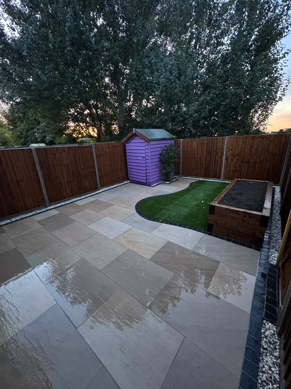 Finished porcelain patio with sleeper bed, turf island and close-board fencing by CG Landscaping