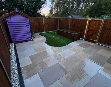 Wide-angle view of finished porcelain patio with kidney-shaped lawn and timber sleeper bed by CG Landscaping