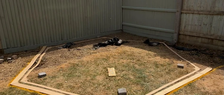 Garden corner before — dry lawn marked out with yellow spray line for the new patio