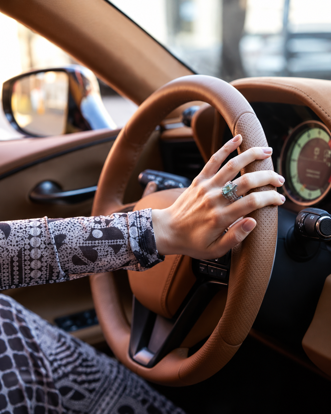 A hand resting on a leather steering wheel, natural nails, no polish.