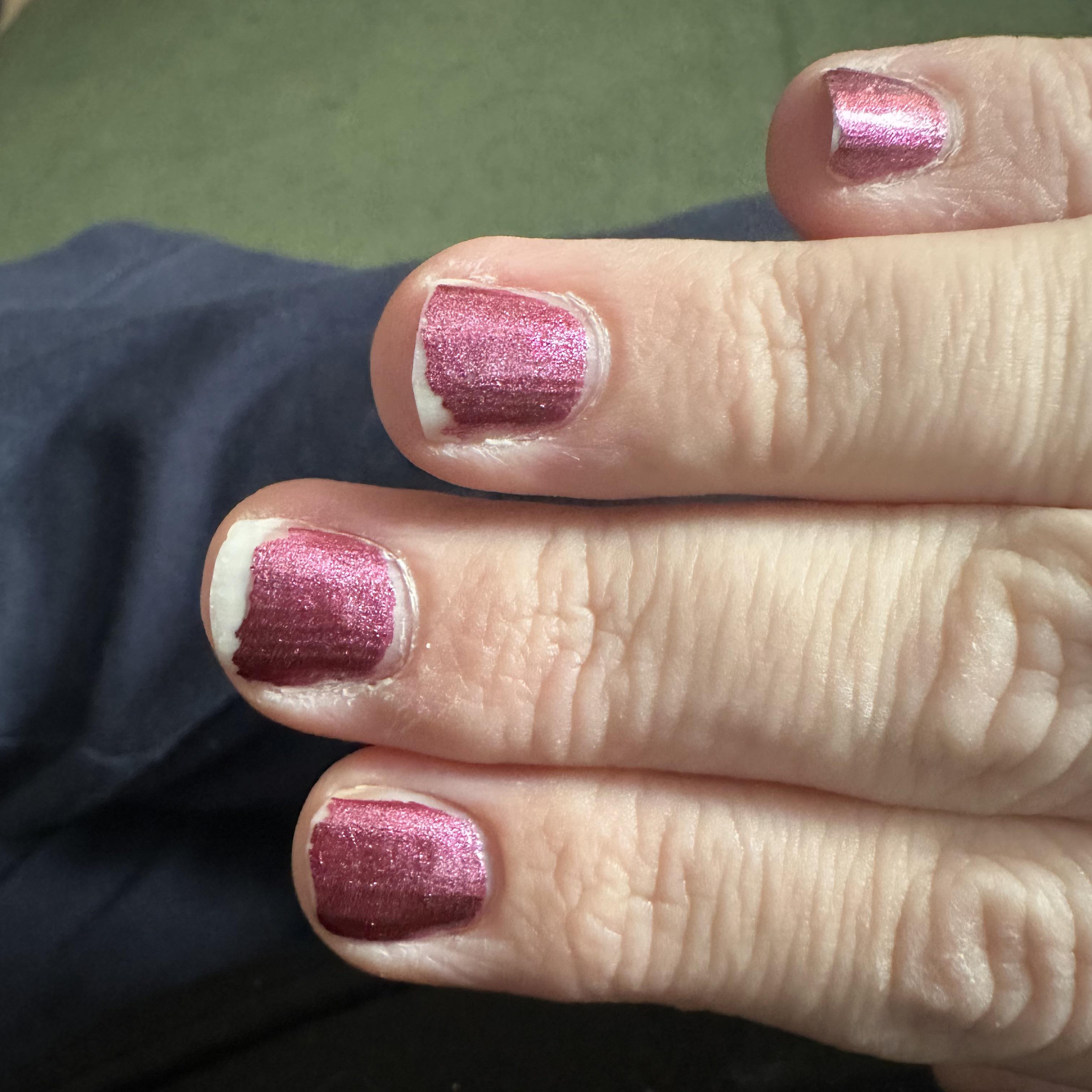 A nail with fresh pink polish still intact, but the edge around it already looks slightly dry and lifted.