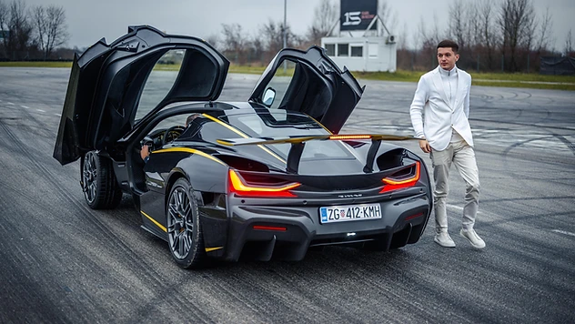 Ein schwarzer Hypercar mit geöffneten Schmetterlingstüren auf einem bewölkten Testgelände.