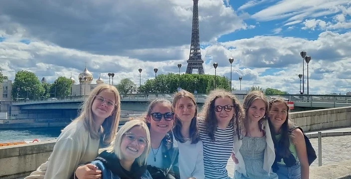 Students from Bovenbouw Sint-Gertrudis Landen sitting on a stone embankment with the Eiffel Tower behind them on a sunny day
