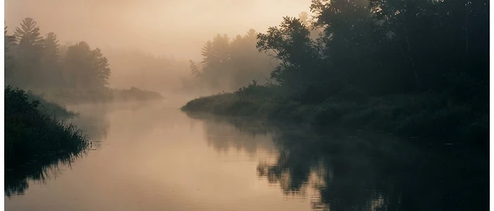 A misty river at early dawn, soft golden light through gentle fog
