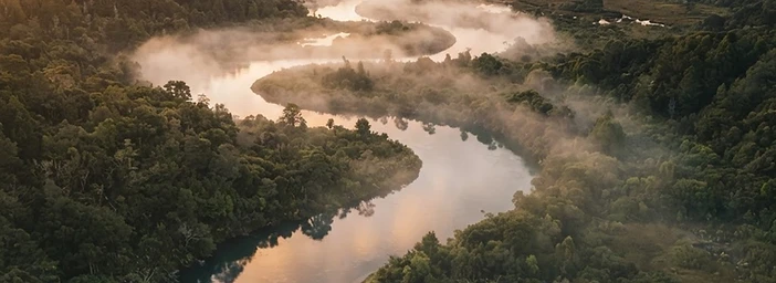 A winding river at golden hour, mist rising over calm water