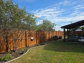 Finished stained long wood fence beside a patio and garden bed