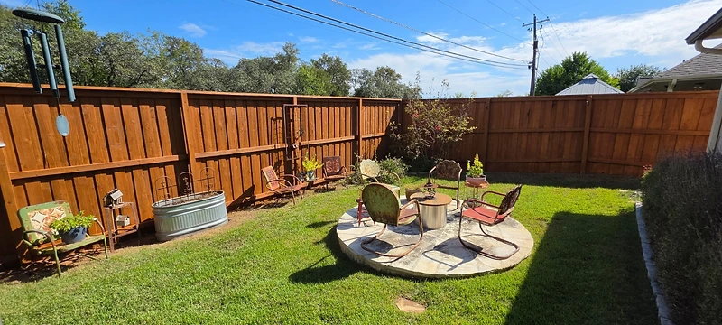 Stained wood fence surrounding a backyard with a circular stone seating area and a fire pit