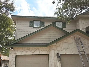 Two-story home after exterior painting, with refreshed cream siding, green trim, and finished garage doors.