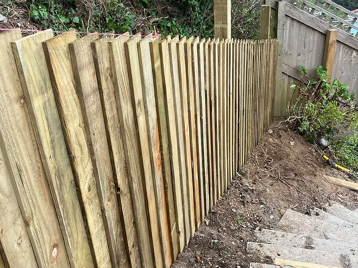 Vertical timber fence pales set to a string line above a stone retaining wall