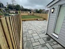 Grey stone patio with lawn, fencing and timber sleeper retaining wall