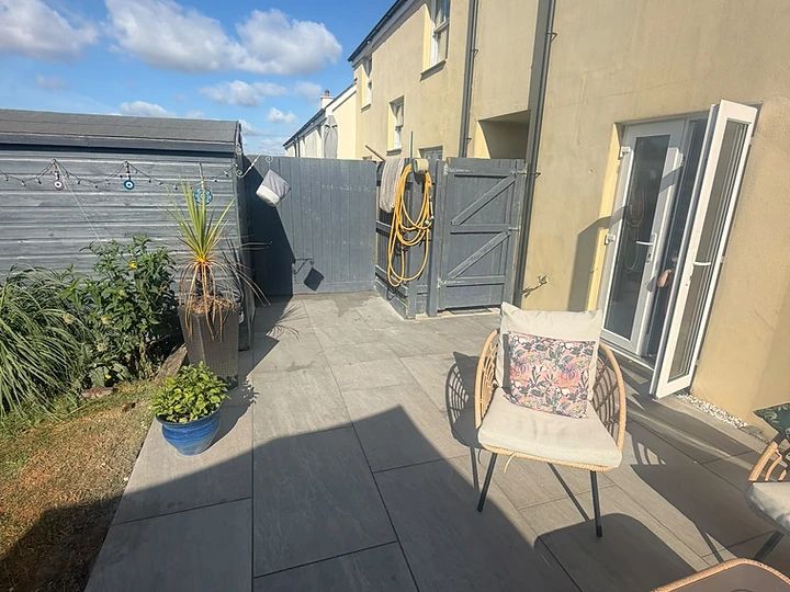 Stone patio with wicker seating and grey-painted boundary fencing