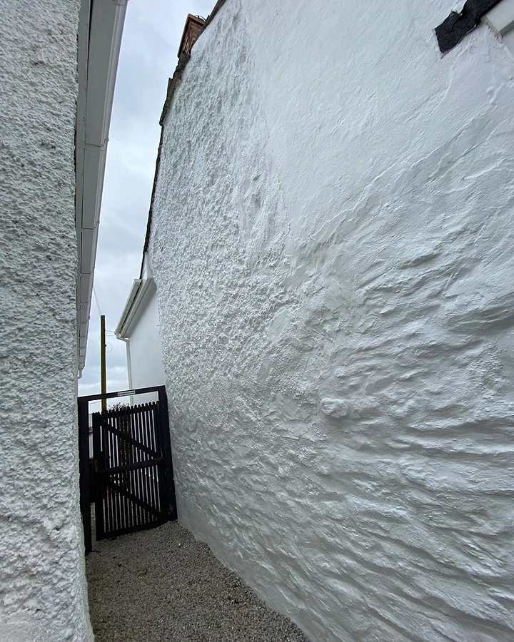 Gravel side passage with rendered walls leading to a black timber gate