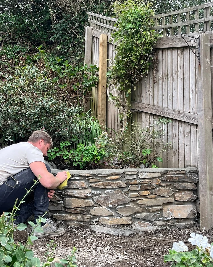 Worker pointing a natural stone retaining wall with a concrete cap
