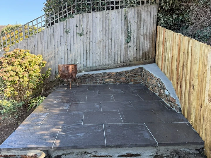 Completed grey stone patio with retaining wall, timber fencing and a fire pit