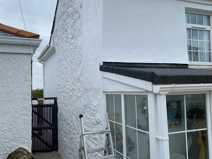 White-rendered house exterior with gravel path during renovation
