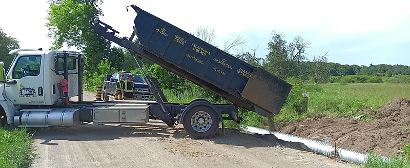 Tor Contracting dump truck delivering fill material into a culvert trench at a rural jobsite