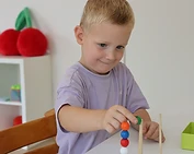 Kind plaatst gekleurde kralen op een houten pinnetje aan een tafel
