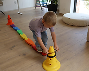 Kind balanceert op een gekleurde balk en plaatst een ring op een kegel