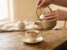 Hands gently pouring tea from a ceramic teapot