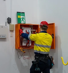 A professional electrician performing safety inspections and maintenance on an electrical switchboard in a workplace environment