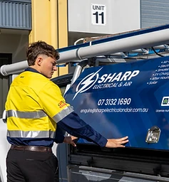 A technician from Sharp Electrical & Air opening a branded utility vehicle to access tools for an electrical service call