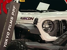 White Jeep Rubicon with aftermarket fenders parked in the TOKYOFILMS PPF installation bay beside branded signage.