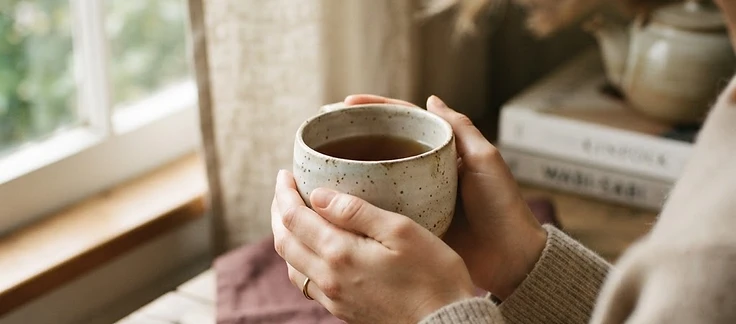 Hands gently cradling a handmade ceramic mug in warm window light