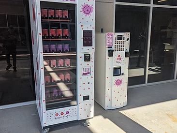 Two donation-station vending machines with pink heart branding deployed outside a glass building