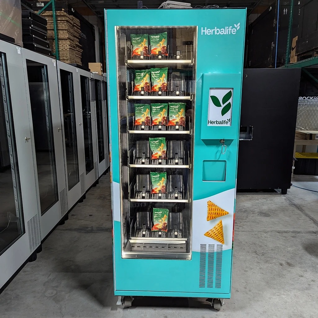 Teal Herbalife branded vending machine stocked with protein chips in a warehouse