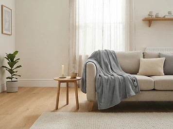 Grijze Warmyy warmtedeken over een lichte linnen bank in een Scandinavische woonkamer
