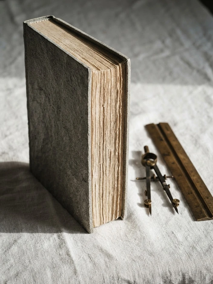 The hardcover book standing beside drafting tools on white linen