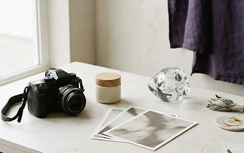 AI-generated conceptual editorial still life of a camera, unbranded product and photographic prints.