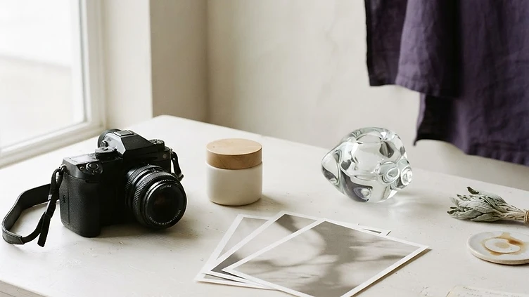 AI-generated conceptual editorial still life of a camera, unbranded product and photographic prints.
