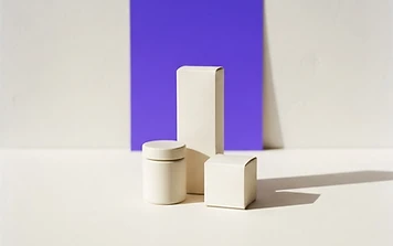 Three carefully arranged ivory product packages against a violet studio panel