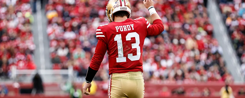 Brock Purdy on the field, finger raised, stadium crowd behind