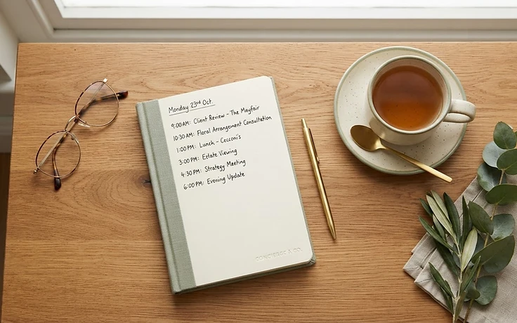 A warm wooden table with glasses, a handwritten schedule, and a cup of tea