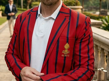 Man wearing a red blazer with navy stripes and an embroidered crest, standing on a stone walkway