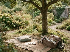 A garden with a mat spread under a tree and a basket of materials beside it