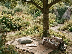 A garden with a mat spread under a tree and a basket of materials beside it